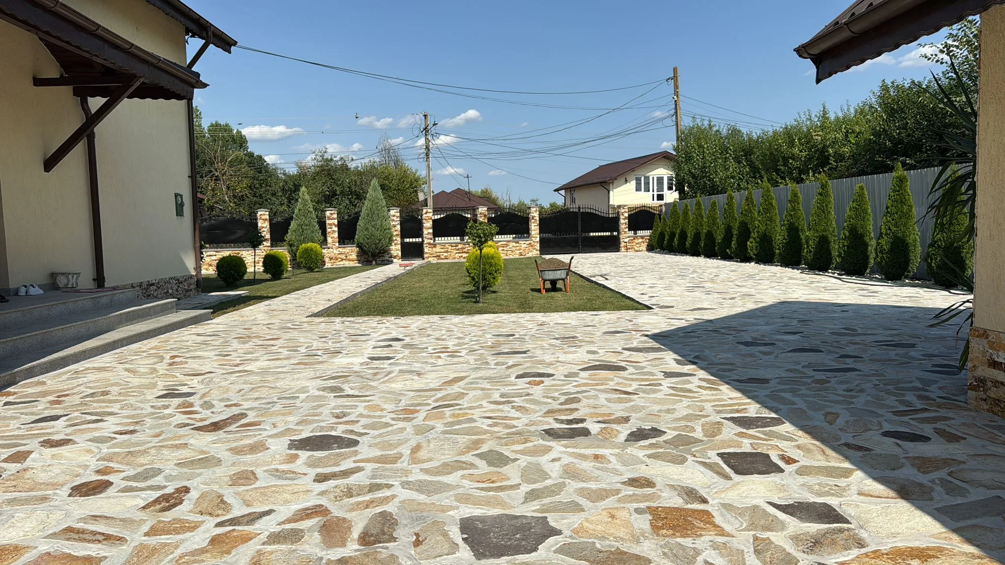 Curte amenajată cu piatră naturală, gazon și conifere.