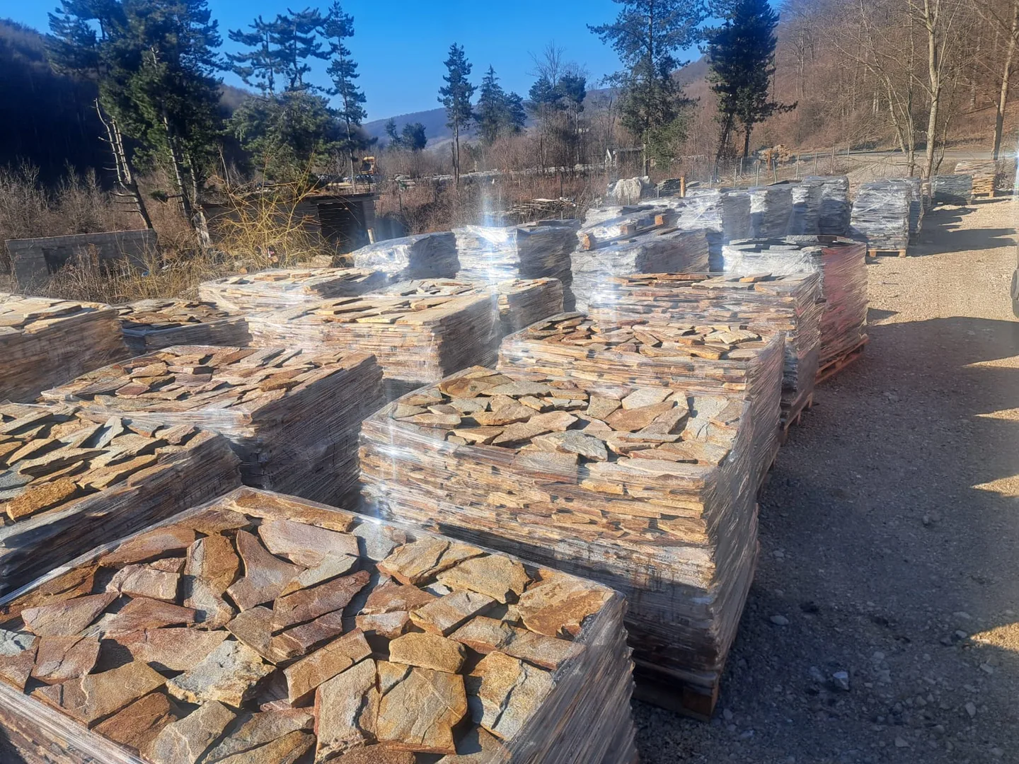 Mai mulți paleți cu piatră naturală într-o zonă exterioară de stocare.
