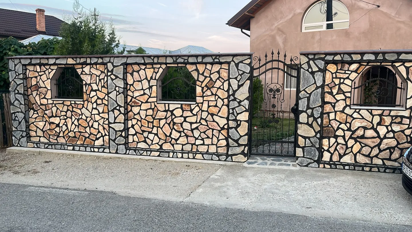 Împrejmuire și stâlpi de poartă placați cu piatră naturală.