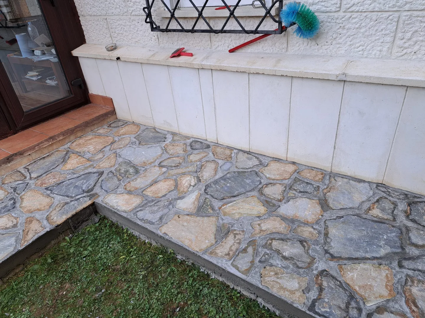 Terasă exterioară placată cu piatră naturală lângă o zonă cu gazon.